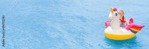Foto Child girl floatting on white and pink trendy beach unicorn on the background of turquoise sea water
