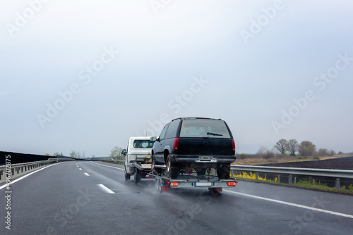 Car carrier trailer with car on wet road. Spray from under the wheels of car.