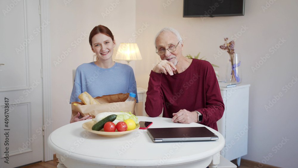 An elderly man and a young girl sit at a table in a large bright room and look at each other An elderly man and a young girl sit at a table in a large bright room and look at each other