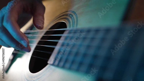 Hand of woman touching strings of guitar performing on stage illuminated by dark purple light. Musician enjoys playing musical instrument extreme closeup