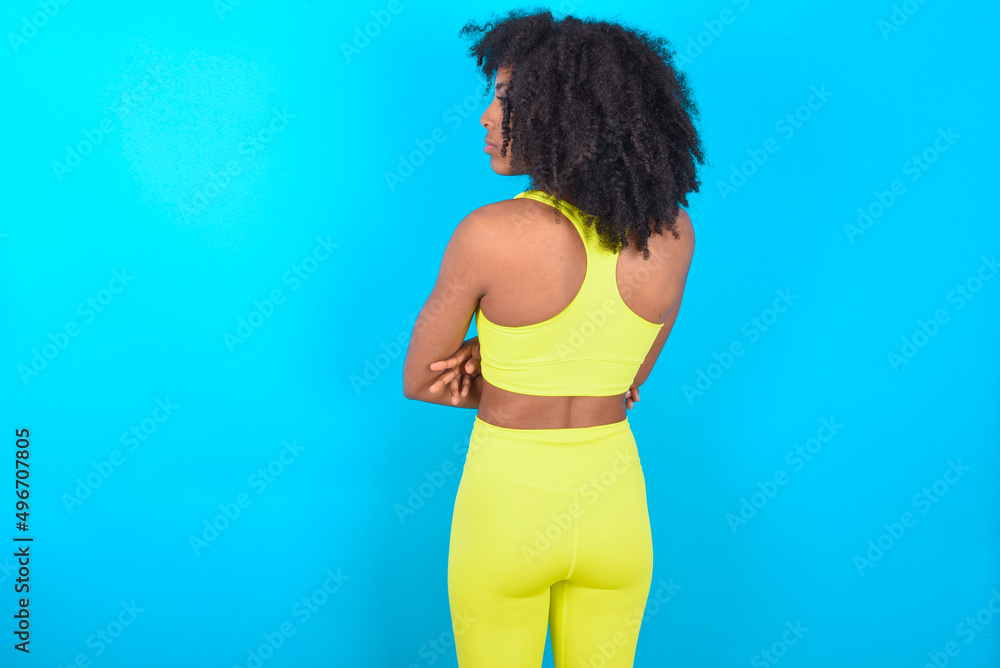 The back view of young woman with afro hairstyle in sportswear against blue background Studio Shoot. The back view of young woman with afro hairstyle in sportswear against blue background Studio Shoot.
