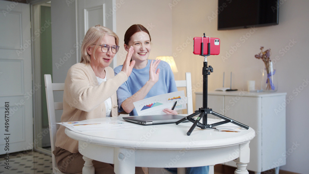 Fototapeta premium Grandmother and her adult daughter tell their business plan using chart sheets. They film themselves on the phone
