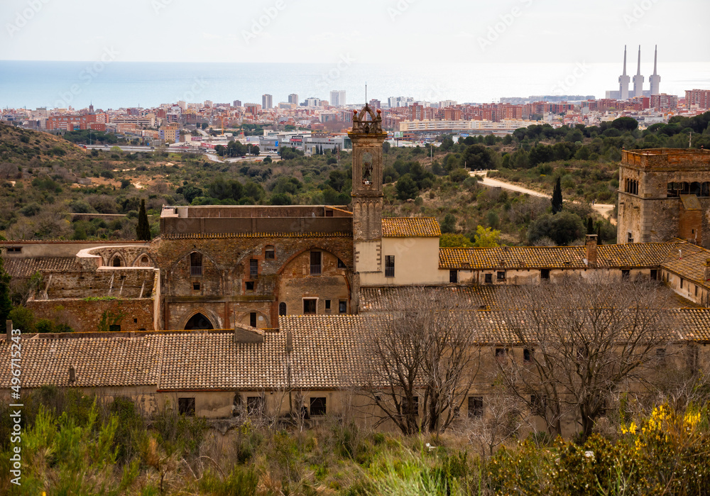 View of ancient Catholic monastery of San Jeronimo de la Murtra on background of Mediterranean coastal city of Sant Adria de Besos with three chimneys of thermal power plant on winter day, Spain