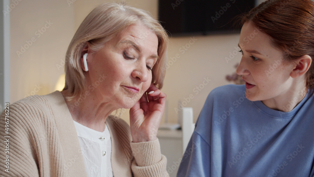 An elderly woman learns to use headphones. She takes the device out of the case and asks her daughter to help An elderly woman learns to use headphones. She takes the device out of the case and asks her daughter to help