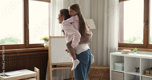 Happy active mum swirls plays with preschooler 5s daughter, cute little girl piggyback mother enjoy funny playtime together in modern nursery room. Carefree weekend leisure with kids at home concept