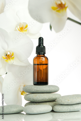 Massage oil and massage stones.Brown glass bottle with massage oil on gray stones and white orchid flower on white background.Spa and aromatherapy.