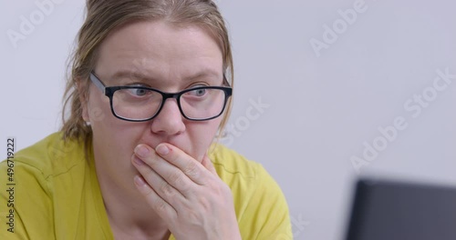 Curvy woman in black-rimmed glasses comes up with idea while working on computer. Sleepy employee sits in office against white wall close view photo