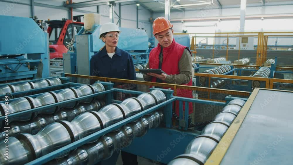 Engineers man and woman with helmet checking talking production process in metal factory. Hard industries. Manufacturing. Walking in warehouse Engineers man and woman with helmet checking talking production process in metal factory. Hard industries. Manufacturing. Walking in warehouse