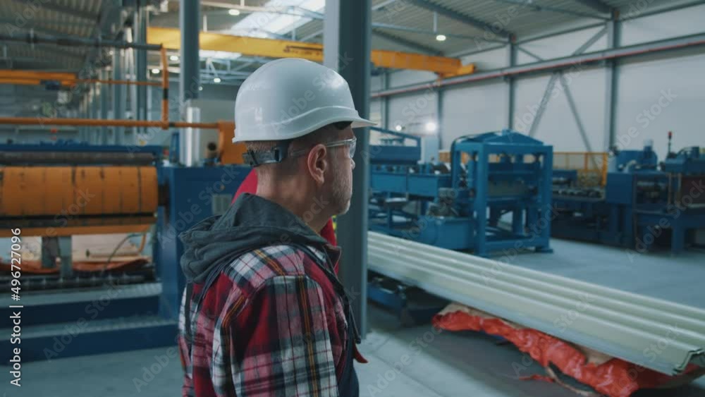 Shot back elder and young engineers men in safety uniform and hard hat talking checks production processes in factory. Inspector in warehouse. Shot back elder and young engineers men in safety uniform and hard hat talking checks production processes in factory. Inspector in warehouse.