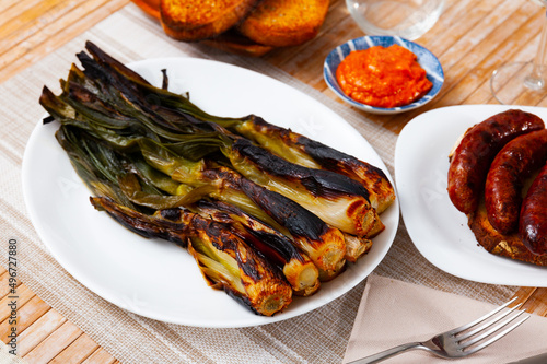 Roasted green onion, calcot, served on table with romesco sauce and botifarra. photo