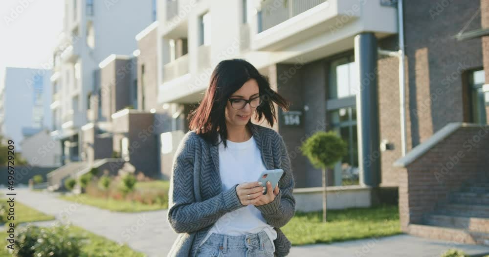Cheerful young caucasian woman typing message at mobile phone during walking at sunny windy weather. Lifestyle, outdoors Cheerful young caucasian woman typing message at mobile phone during walking at sunny windy weather. Lifestyle, outdoors