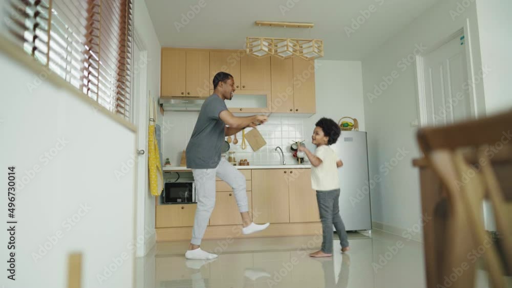 Happy relaxed black African American Father and his little afro boy dancing while cooking in the kitchen at home. Happy relaxed black African American Father and his little afro boy dancing while cooking in the kitchen at home.