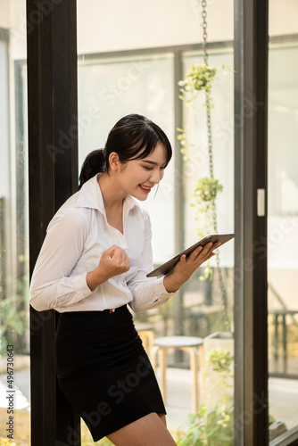 Asian woman holding a touchpad while standing in the office with large glass windows A female manager uses digital pads to organize her work. Free Download Asian woman holding a touchpad while standing in the office with large glass windows A female manager uses digital pads to organize her work. - GFXLoad