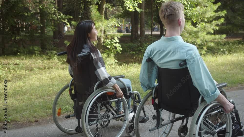 Two disabled young friends are walking in the forest, rolling down the road and talking Two disabled young friends are walking in the forest, rolling down the road and talking