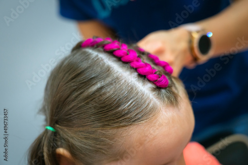 The hairdresser weaves a pink kanekalon into the girl's braids. High quality photo