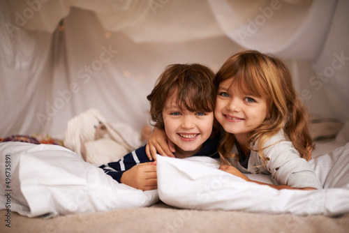 Siblings make the best of friends. Shot of two adorable siblings lying in their blanket fort indoors.