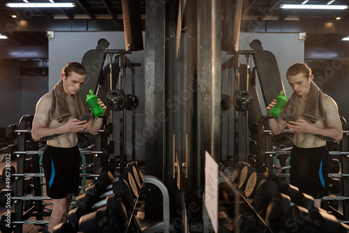 Fit serious sportsman drinking water and checking social media on smartphone between exercise sets in gym © DragonImages