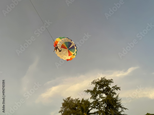 Parasailing, parascending, paraskiing, parakiting, Parachute with two people in the clear blue sky. Close-up, isolated, macro. Tree, clouds. Extreme sport. Flight in the skies. Soar at heaven. Fun