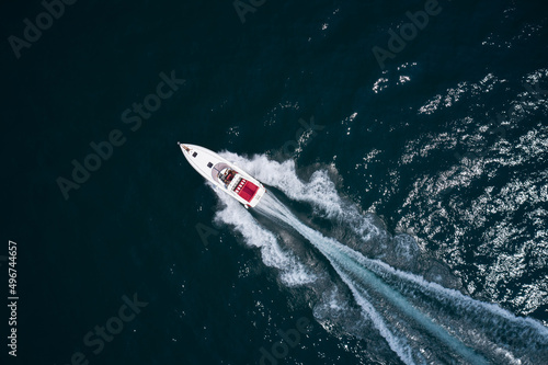 Drone view of a moving white boat on the water. People rest on a boat. Speedboat moves fast on the water top view. Speed boat with red seats aerial view. © Berg