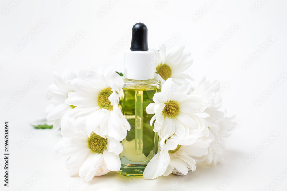 Close up of a glass bottle with cosmetic decorated with chamomile flowers. White background. The concept of organic natural cosmetics