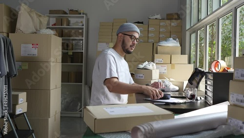 Asian man online seller confirming orders from customer on the phone. E-commerce business owner looking at the phone in store warehouse.