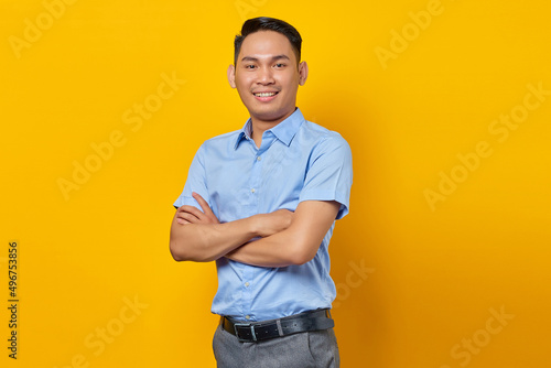 portrait of smiling young asian man in glasses holding hands together and feels optimistic isolated on yellow background. businessman and entrepreneur concept