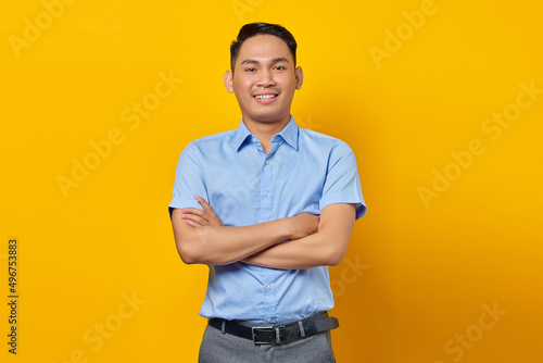portrait of smiling young asian man in glasses holding hands together and feels optimistic isolated on yellow background. businessman and entrepreneur concept