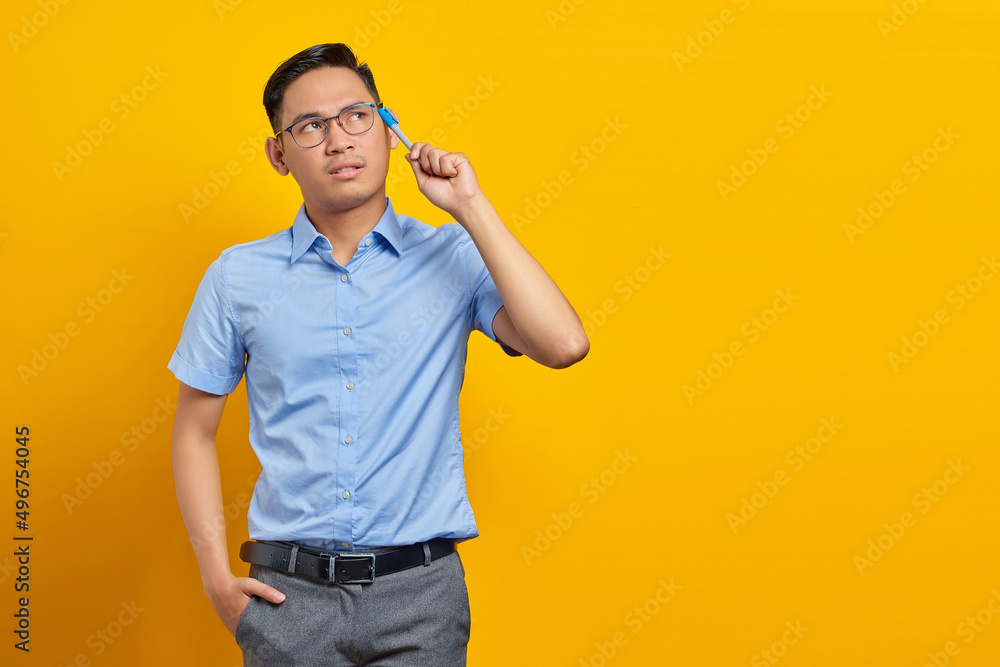 portrait of pensive young asian man in glasses looking seriously thinking about a question isolated on yellow background. businessman and entrepreneur concept portrait of pensive young asian man in glasses looking seriously thinking about a question isolated on yellow background. businessman and entrepreneur concept