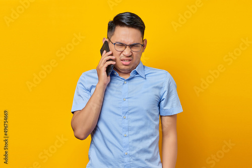 Angry young asian man Asian in glasses talking on mobile phone isolated on yellow background. businessman and entrepreneur concept