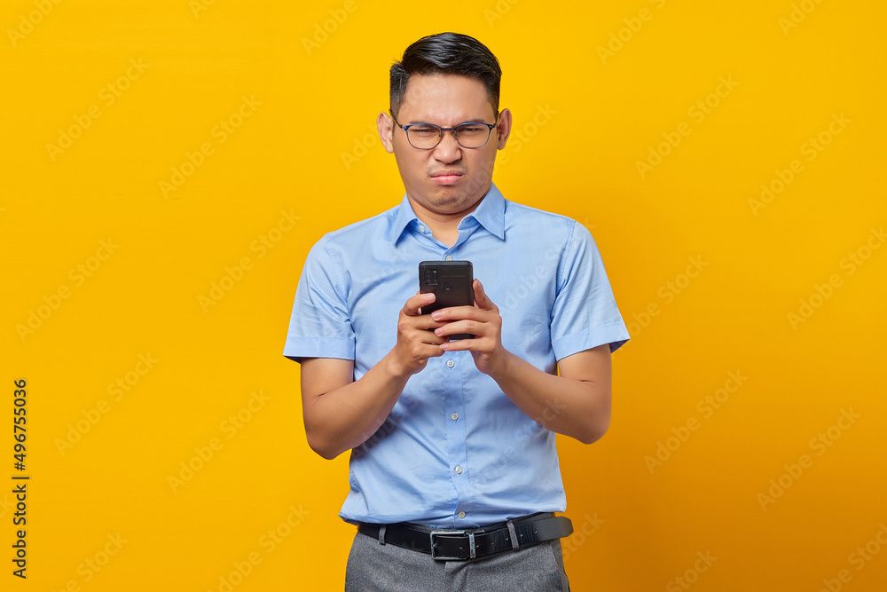 Pensive young asian man Asian in glasses reply to incoming messages on mobile Phone isolated on yellow background. businessman and entrepreneur concept Pensive young asian man Asian in glasses reply to incoming messages on mobile Phone isolated on yellow background. businessman and entrepreneur concept