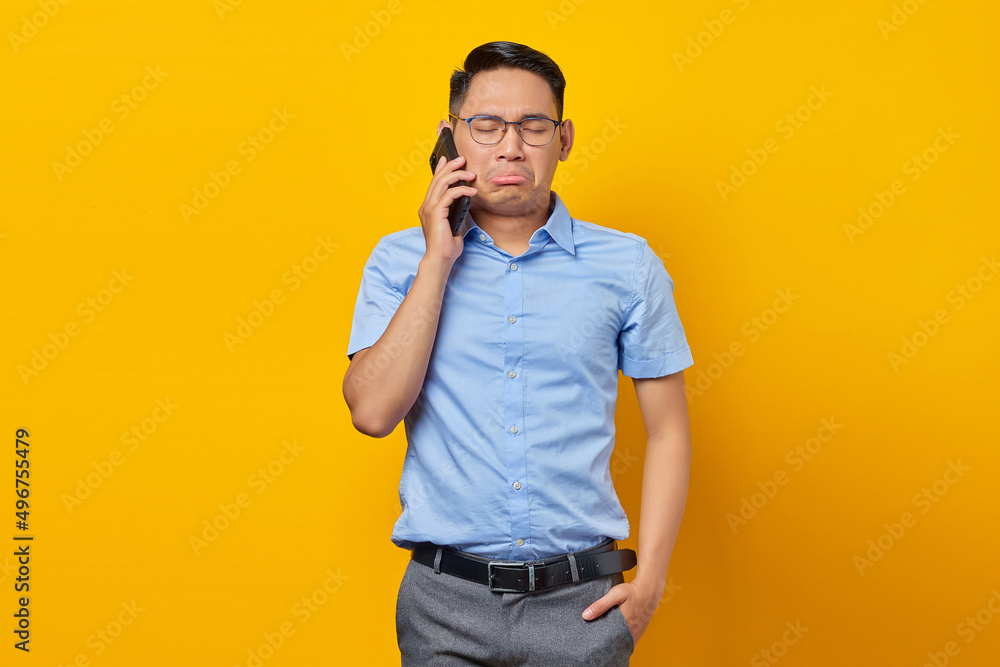 Sad young asian man Asian in glasses talking on mobile phone isolated on yellow background. businessman and entrepreneur concept Sad young asian man Asian in glasses talking on mobile phone isolated on yellow background. businessman and entrepreneur concept