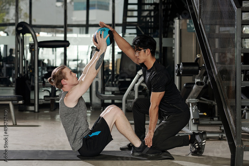 Fitness instructor holding feet of client who is doing sit-ups and lifting medicine ball