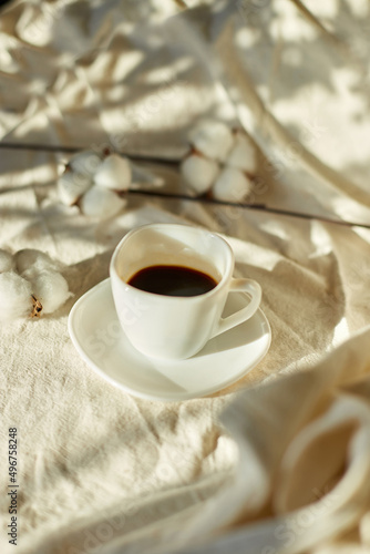 Cup of coffee in bed with cotton flowers, morning mood, Organic and natural linen cotton textile bedclothes, copy space.