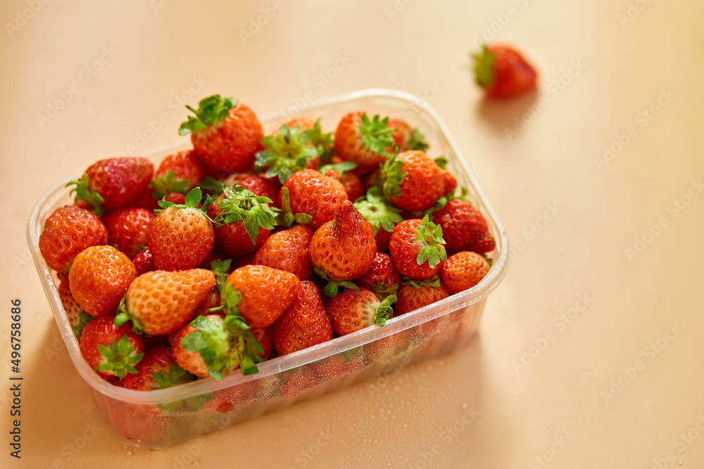Red ripe organic strawberries in plastic tray container on orange background, copy space for text, top view, market local farm concept, harvest. Red ripe organic strawberries in plastic tray container on orange background, copy space for text, top view, market local farm concept, harvest.