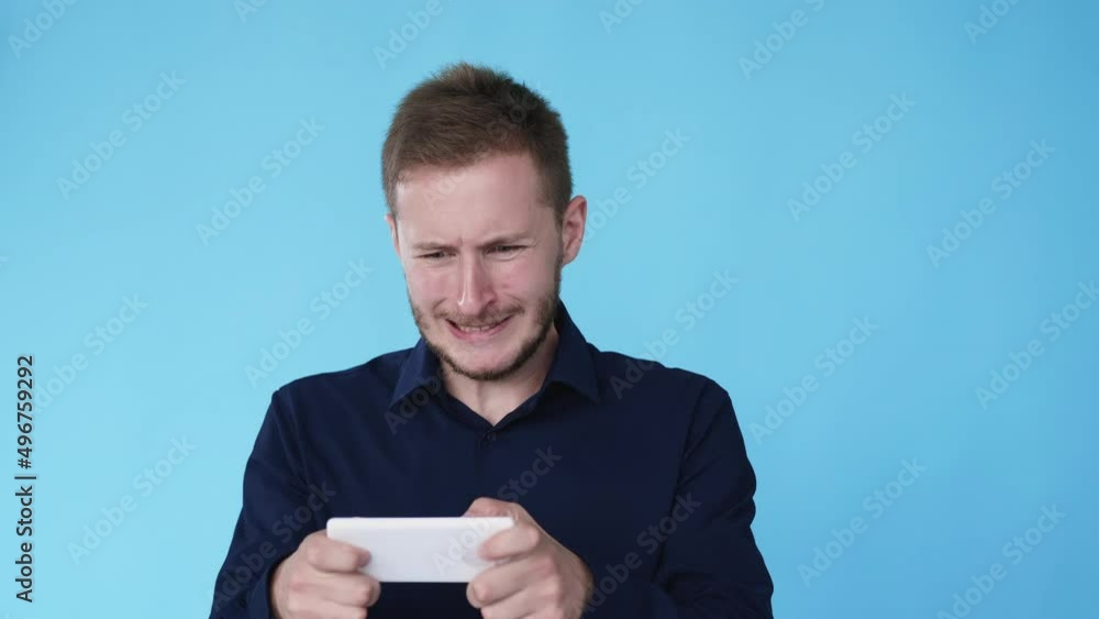 Phone gaming. Gadget addiction. Smartphone nerd. Mobile entertainment. Boomerang motion. Concentrated man playing game on cell isolated on blue background GIF loop animation. Phone gaming. Gadget addiction. Smartphone nerd. Mobile entertainment. Boomerang motion. Concentrated man playing game on cell isolated on blue background GIF loop animation.