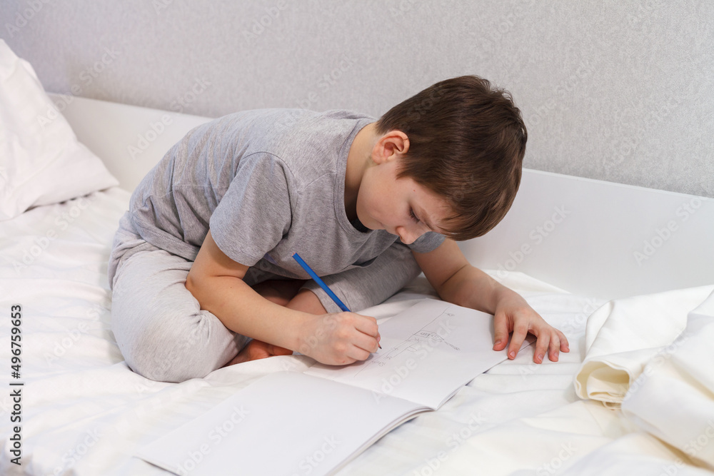 The child draws with a pencil on paper while sitting on the bed, close-up. Hobby The child draws with a pencil on paper while sitting on the bed, close-up. Hobby