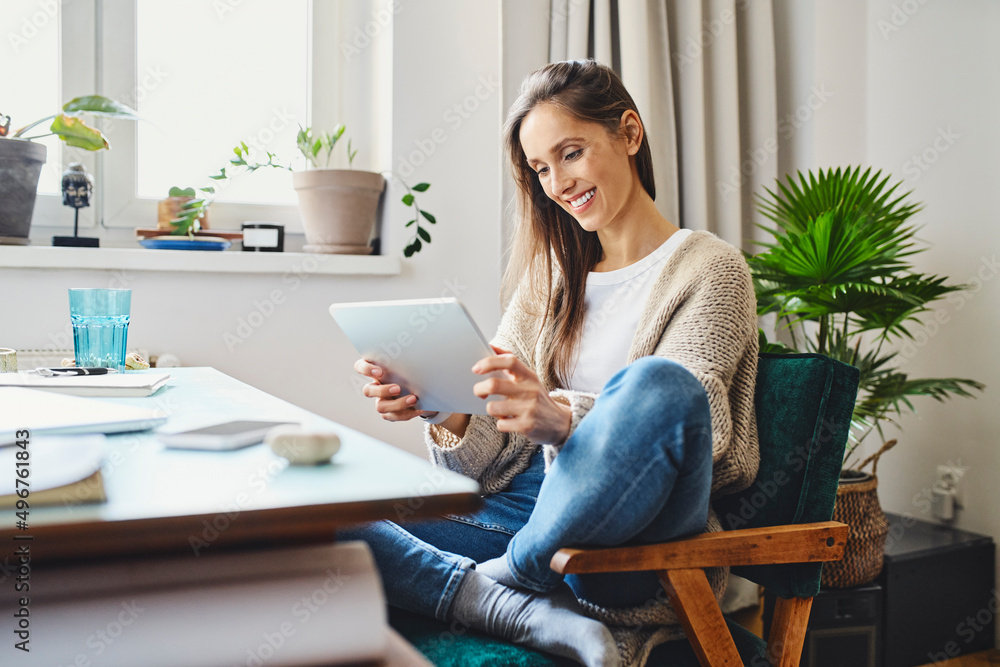 Smiling woman using tablet PC sitting on chair at home Smiling woman using tablet PC sitting on chair at home