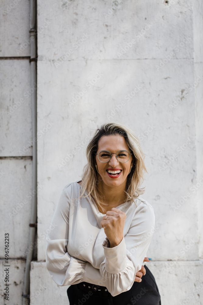 Cheerful woman clenching fist in front of wall Cheerful woman clenching fist in front of wall