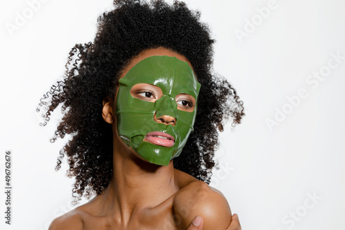 Young woman with facial mask on face against white background photo