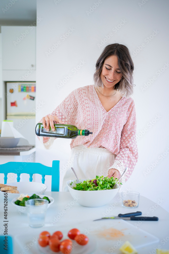 Smiling young woman pouring olive oil in salad bowl at table Smiling young woman pouring olive oil in salad bowl at table