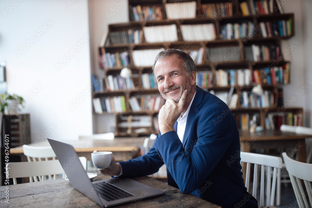 Smiling businessman with coffee cup and laptop sitting at table in cafe Smiling businessman with coffee cup and laptop sitting at table in cafe