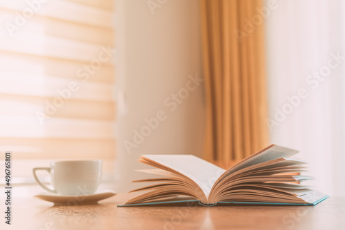 Open book and coffee cup on the table, reading at home in the morning