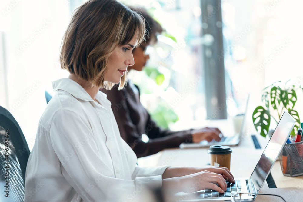 Businesswoman with colleague using laptop at desk in office Businesswoman with colleague using laptop at desk in office