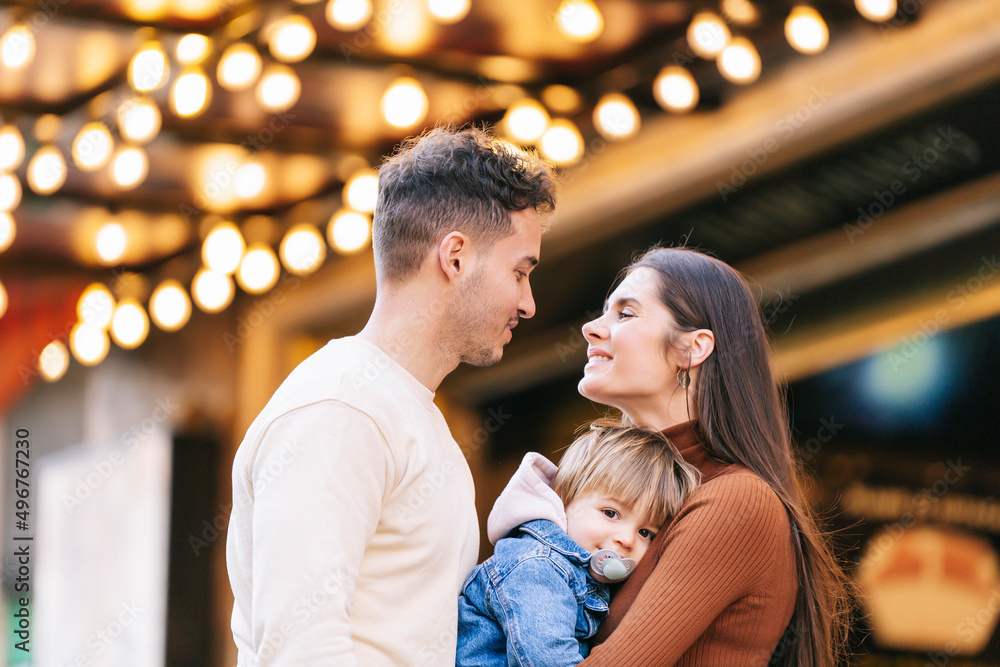 Smiling young woman carrying son looking at man in front of illuminated ceiling Smiling young woman carrying son looking at man in front of illuminated ceiling