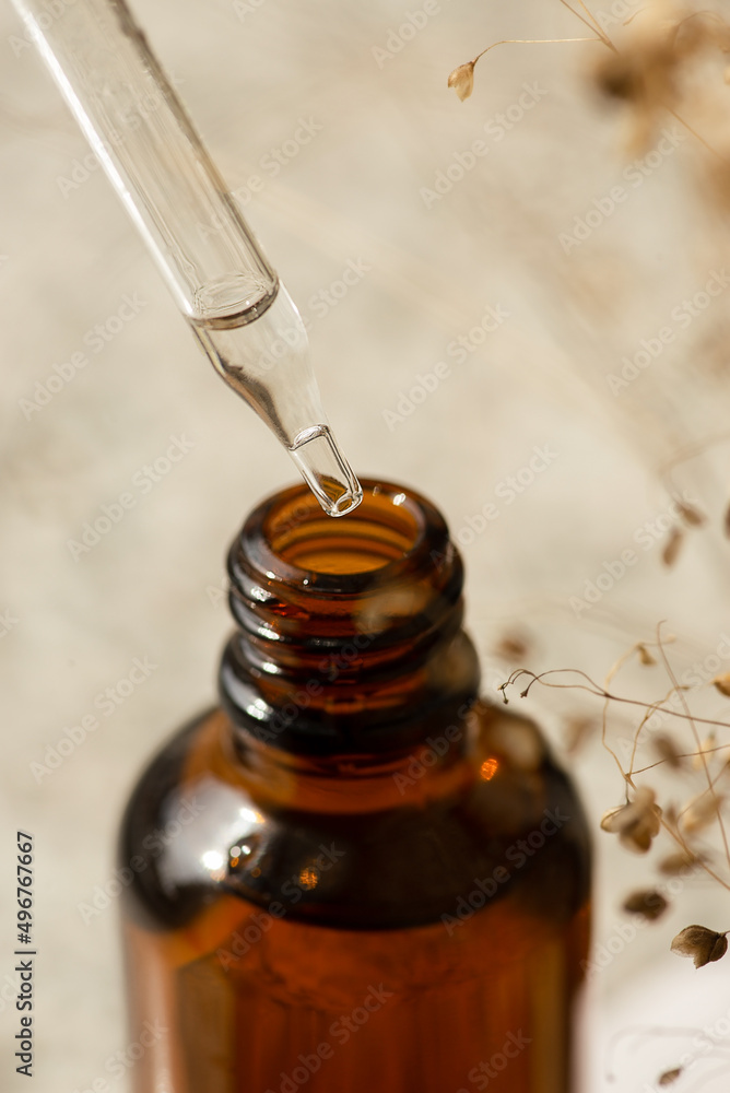 Pipette close-up with serum or oil and an amber bottle. Skincare products, natural cosmetic. Beige background with daylight and dry plant. Beauty concept for face and body care Pipette close-up with serum or oil and an amber bottle. Skincare products, natural cosmetic. Beige background with daylight and dry plant. Beauty concept for face and body care