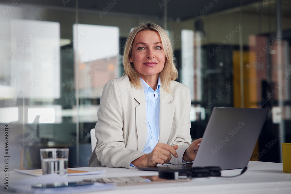 Smiling businesswoman with laptop at desk in office Smiling businesswoman with laptop at desk in office