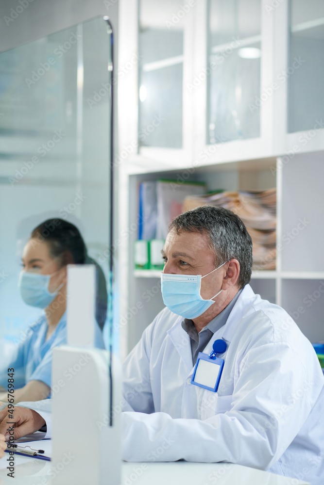 Senior doctor in medical mask working at clinic reception, consulting patients and filling forms Senior doctor in medical mask working at clinic reception, consulting patients and filling forms