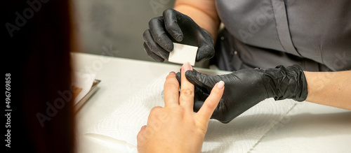Close up of the caucasian hands of a professional manicurist are filing the nails of a young woman. Young caucasian woman receiving a manicure by a beautician with a nail file in a nail salon photo