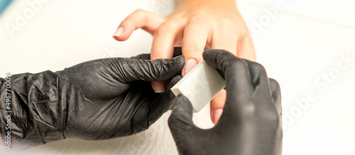 Close up of the caucasian hands of a professional manicurist are filing the nails of a young woman. Young caucasian woman receiving a manicure by a beautician with a nail file in a nail salon photo