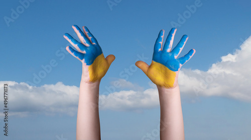 Child's hands painted in the colors of the national flag of Ukraine on blue sky background.